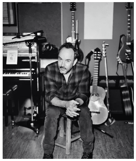 A man sitting in front of some guitars and other musical instruments.